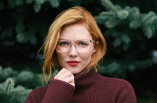 Une femme rousse portant des lunettes rose transparente et un col roulé bourgogne