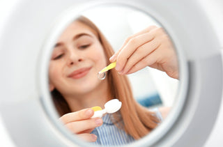 Devant un miroir, une adolescente sort ses lentilles de contact de leur étui.