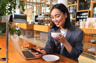 Femme d'affaires souriant en regardant son téléphone intelligent tout en buvant un café dans un cybercafé. 