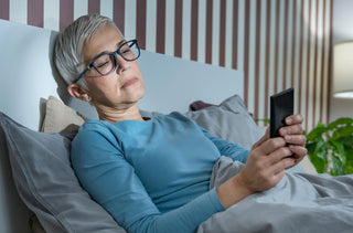 Femme aux cheveux blancs courts regardant son téléphone au lit.