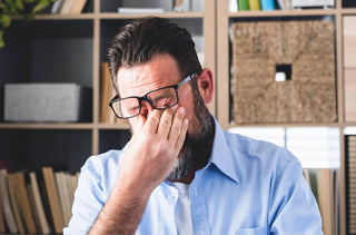 Homme qui se frotte les yeux sous ses lunettes à cause de sécheresse oculaire