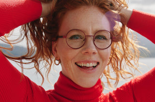 Une femme rousse portant des lunettes rondes rouges et un col roulé rouge