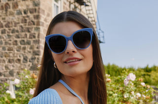 Une femme qui porte une paire de lunettes de soleil bleu de Kate Spade. 