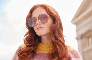 Une femme porte des lunettes de soleil géométriques roses et dorées de chez Chloé.