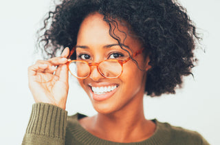 Une femme sourit et tient ses lunettes de prescription dans sa main