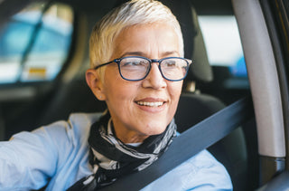 Femme aux cheveux blancs portant des lunettes, assise dans une voiture avec sa ceinture de sécurité