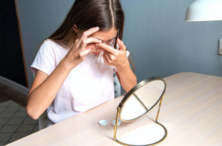 Une jeune fille met ses lentilles cornéennes devant un petit miroir rond