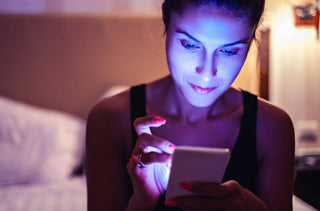 Une femme assise sur le bout de son lit regarde son cellulaire