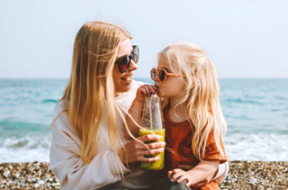 Une jeune fille boit un smoothie avec sa mère à la plage. Toutes les deux portes des lunettes de soleil. 