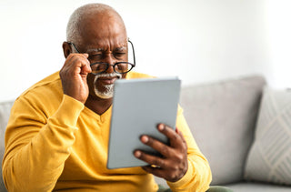 Un vieil homme noir qui portent un chandail jaune et des lunettes noires a de la difficulté à lire sa tablette