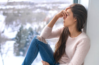 Une femme assise sur un grand rebord de fenêtre, une main couvrant ses yeux, se sent stressée, anxieuse. Elle souffre de dépression saisonnière.