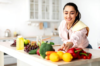 Une femme souriante attrape les légumes frais étalés devant elle sur l'îlot de cuisine pour préparer une salade.