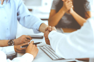 Gros plan sur 4 personnes assises à un bureau, dont 2 se serrent la main.