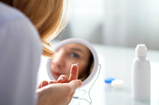 Une femme met ses lentilles cornéennes devant un petit miroir de maquillage rond.