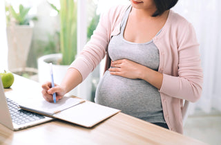 Une femme enceinte écrit dans son carnet de notes à son bureau.