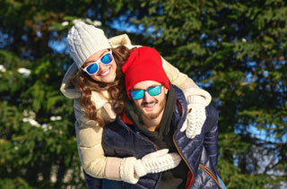 Vêtus d'habit d'hiver et de lunettes de soleil, un couple s'amuse dans un parc. L'homme tient la femme sur son dos. 