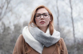 Une femme rousse portant des lunettes noires et un manteau d'hiver avec une écharpe blanche et grise.