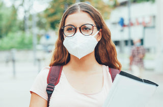 Une femme porte un masque blanc à l'extérieur.