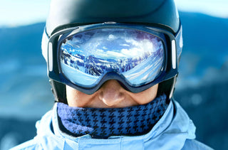 gros plan sur les lunettes de ski d'un homme dans lesquels nous pouvons voir la réflexion des montagnes enneigées 