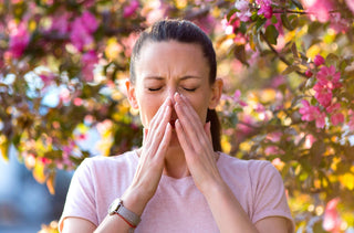 Une femme éternue devant un arbre en fleur à cause de ses allergies saisonnières