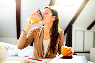 Portrait d'une femme assise à son bureau qui boit un jus d'orange