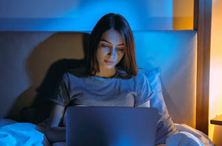 Une femme assis dans son lit avec son ordinateur portable