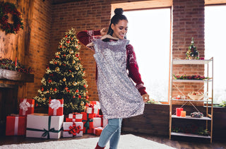 Sous un décor de Noël, une femme tient une robe argentée scintillante devant elle