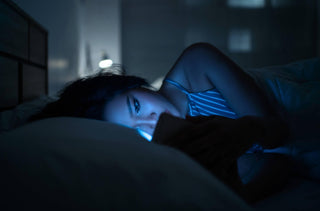 Une femme couchée dans son lit regarde son cellulaire dans le noir