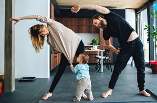 Famille faisant du yoga. La mère et le père font des inclinaisons latérales, tandis que leur enfant tire le chandail de sa mère, cherchant de l'attention.