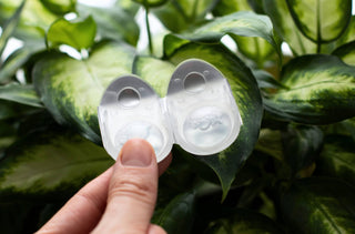 Une personne tient des lentilles cornéennes devant des plantes vertes