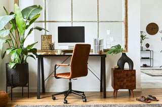 Un espace de travail élégant avec un bureau industriel noir, un fauteuil en cuir marron, un ordinateur, des plantes, etc.