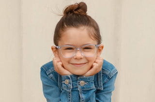 Une jeune fille portant une veste en jean et des lunettes transparentes sourit à la caméra.