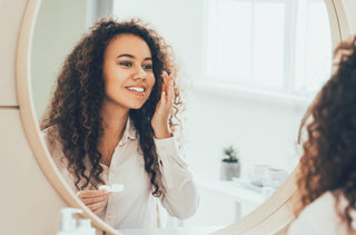 Une femme insère ses lentilles cornéennes devant le miroir de la salle de bain.