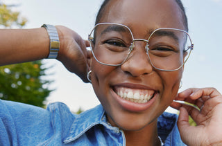 Une jeune femme avec des lunettes surdimensionnés sourit