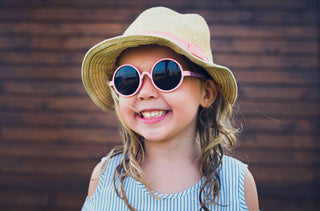 Une jeune fille souriante porte des lunettes de soleil et un chapeau