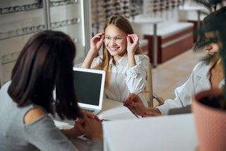 Essayage de lunettes de vue en magasin d’optique avec une conseillère et une cliente souriante
