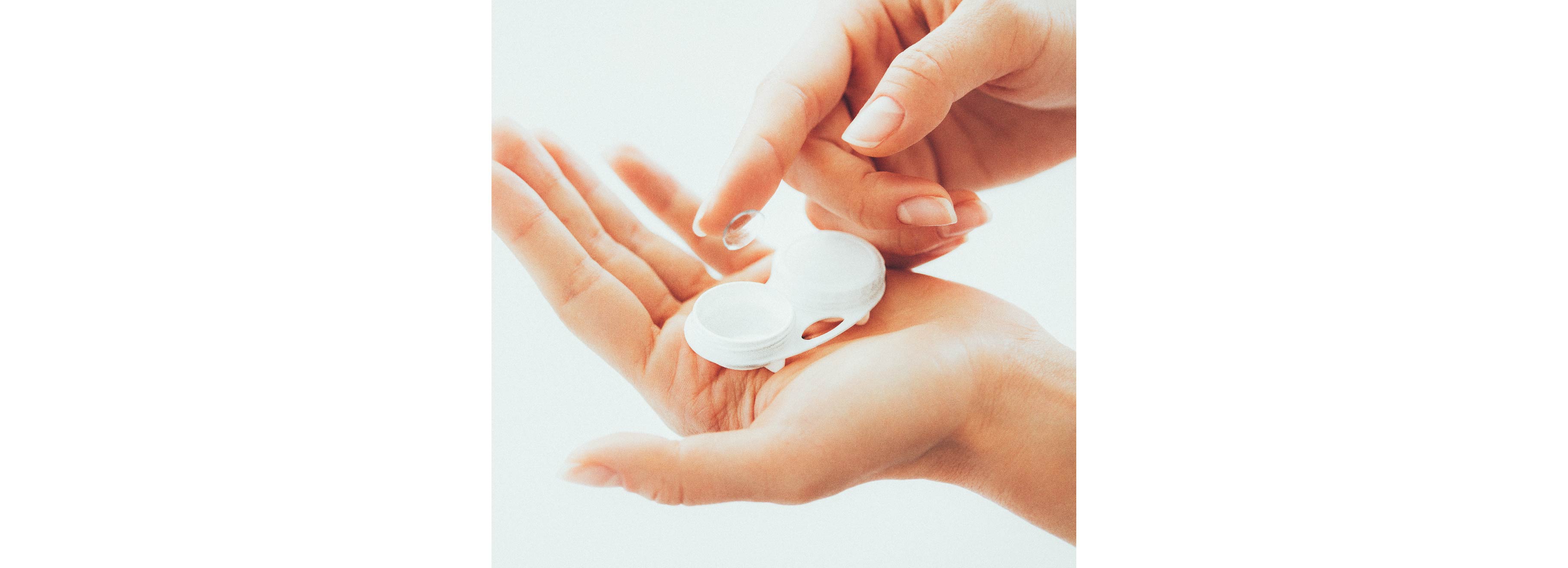 A hand is holding a contact lens case filled with cleansing liquid