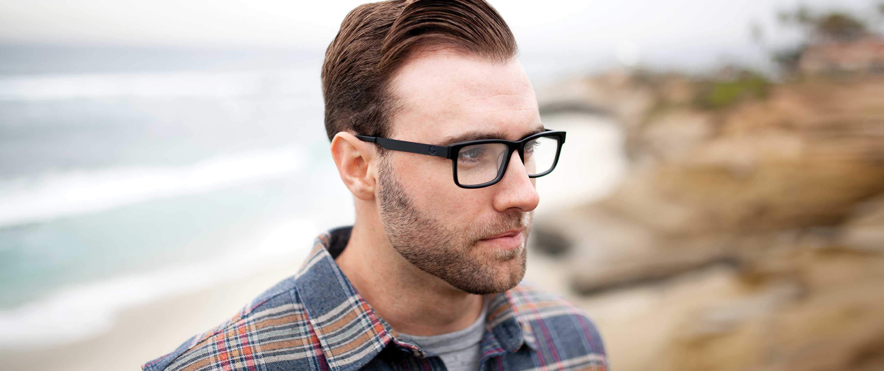 A man is on the beach, wearing SPY optical glasses