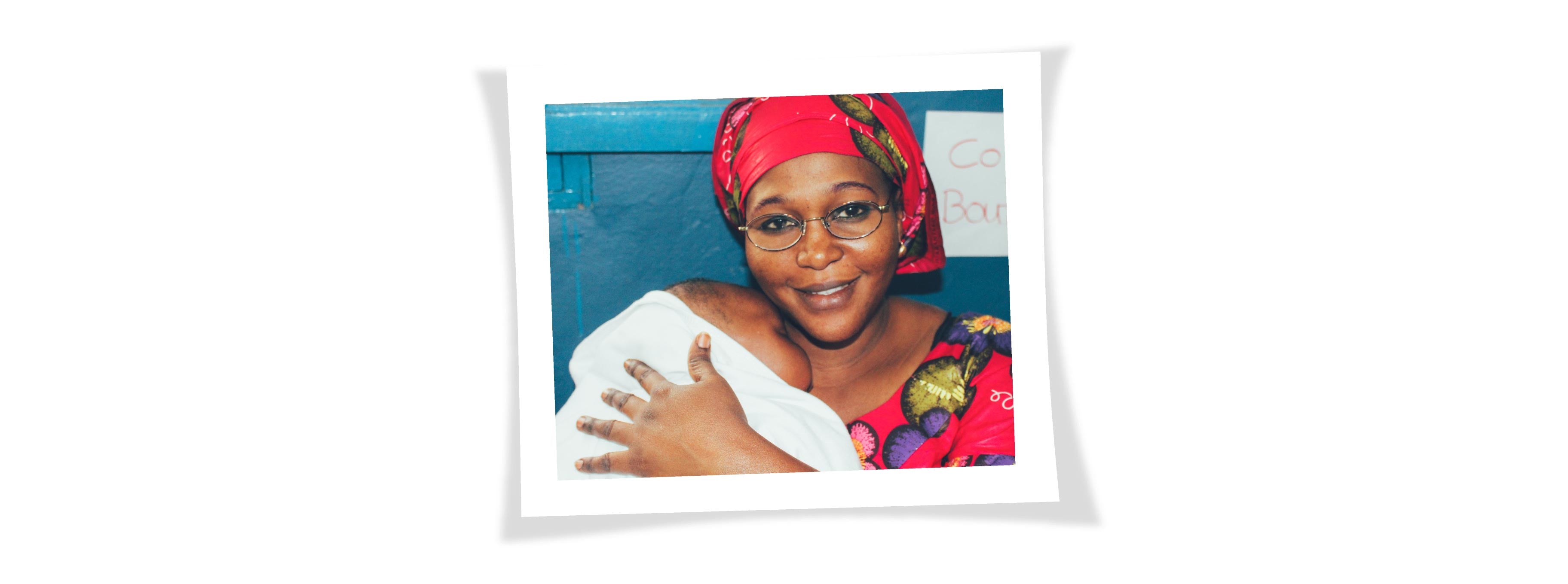 A Senegalese woman is holding her baby in her arms and she is wearing the glasses that were given to her by IRIS Mundial 