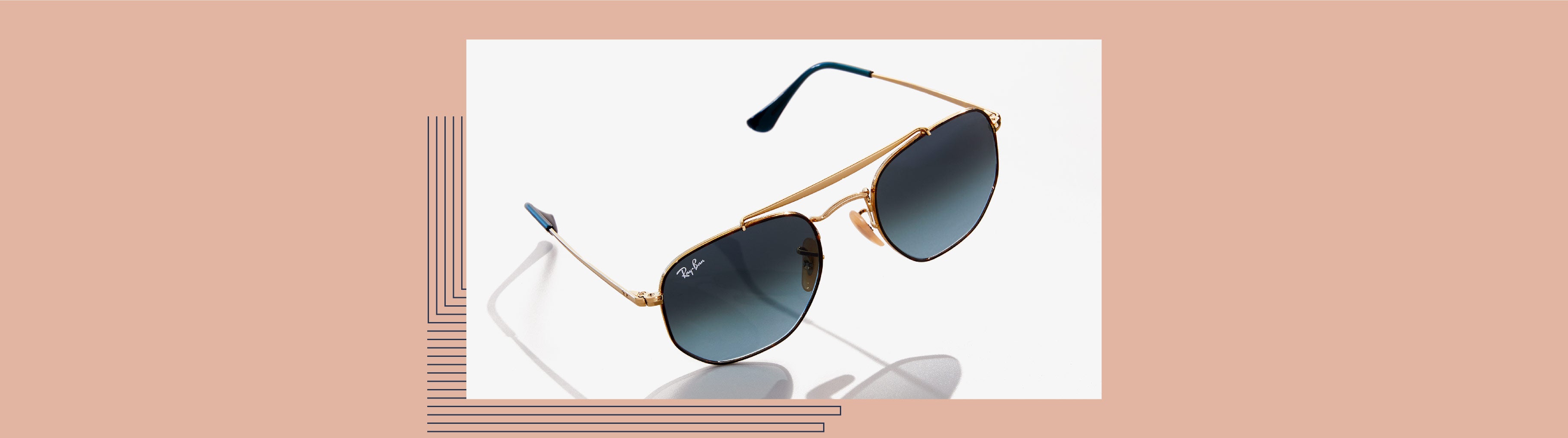 Paire de lunettes solaires Ray Ban avec un double pont doré sur un fond rose saumon.