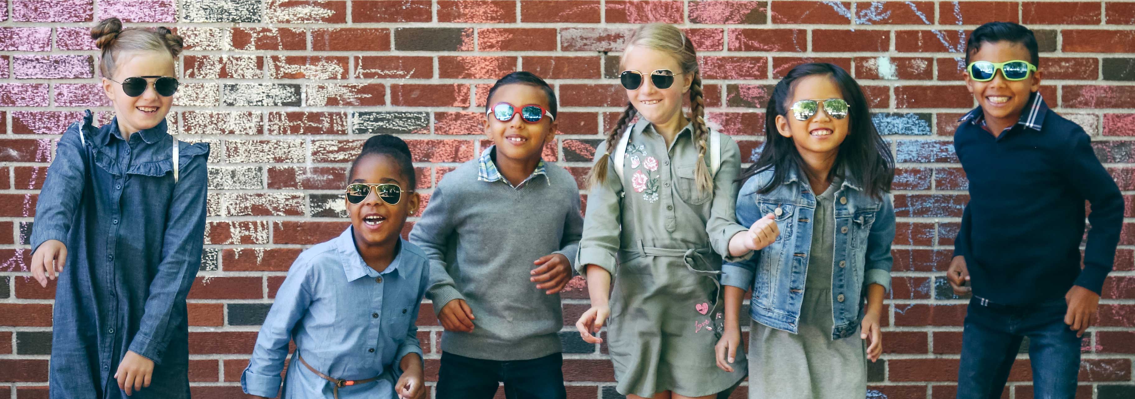 Young children are wearing glasses and sunglasses in the school yard, they are jumping all at once and are laughing